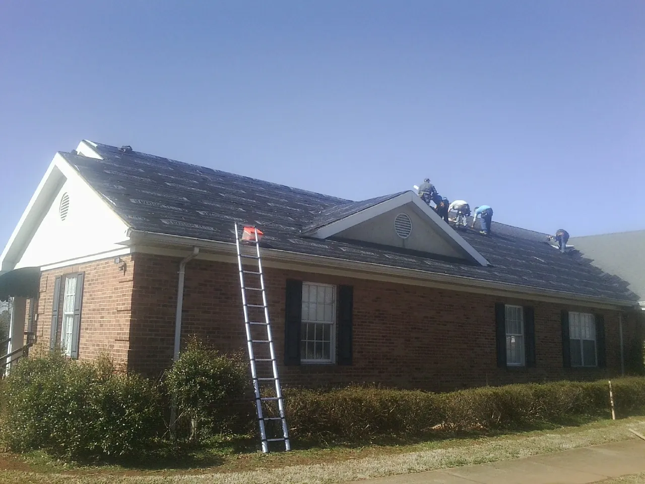 Crew tearing shingles off a brick ranch roof with a ladder set — Emergency Roof Repair work by our crew in Worden