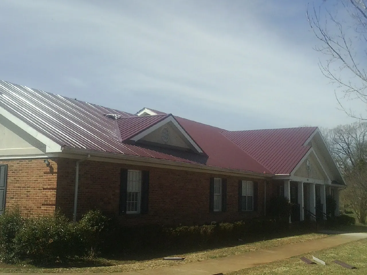 Red metal roof with gabled entries on a long brick building, from a Hail Damage Roof Repair job in Worden