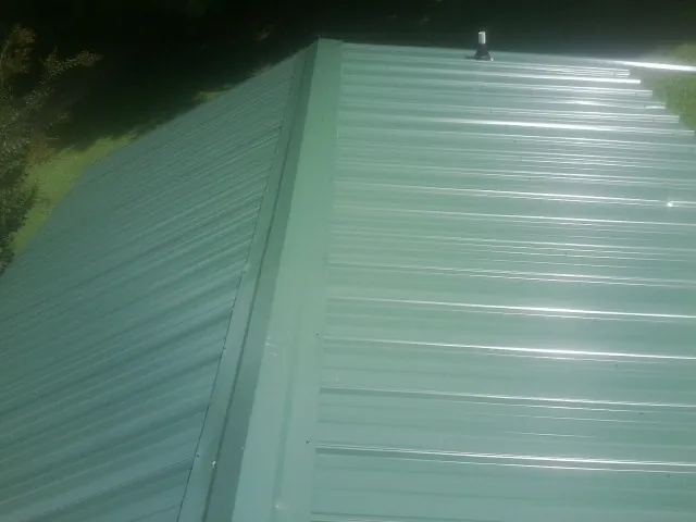New green metal panels meeting at the ridge of a roof — Flat Roof Repair work by our crew in Worden