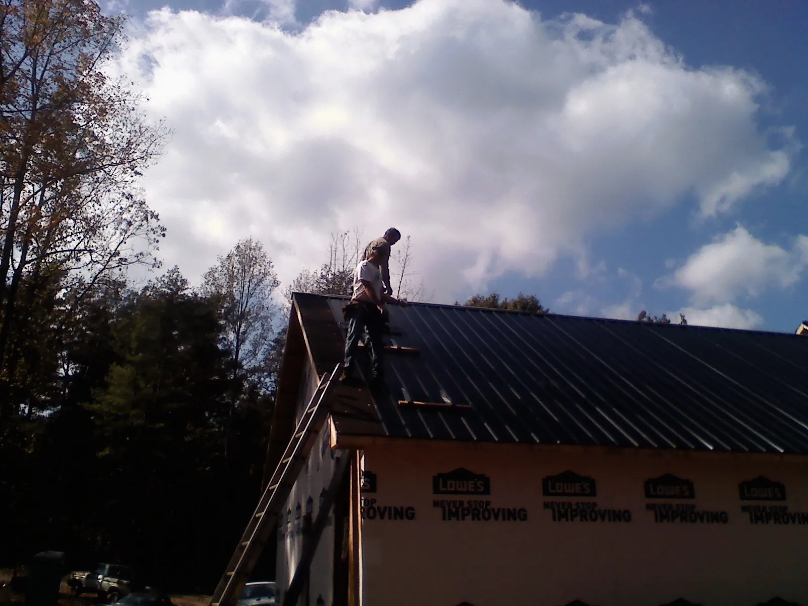Roofer fastening dark metal panels high against a cloudy sky, from a Roof Inspection job in Worden